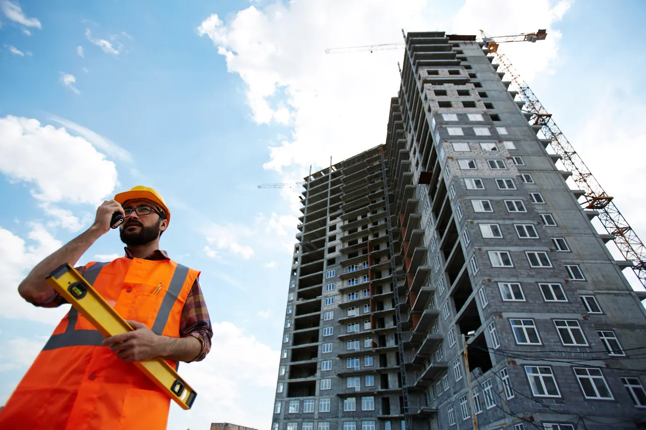 Site engineer with a level in front of a high-rise under construction